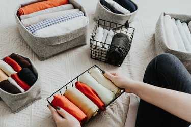 Folding clothes and organizing stuff in boxes and baskets. Concept of tidiness, minimalist lifestyle and japanese t-shirt folding system.