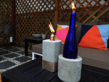 DIY concrete tabletop tiki torches out of used glass bottles on outdoor coffee table.