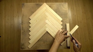 Measuring and cutting paint stir sticks to tabletop to create herringbone pattern.